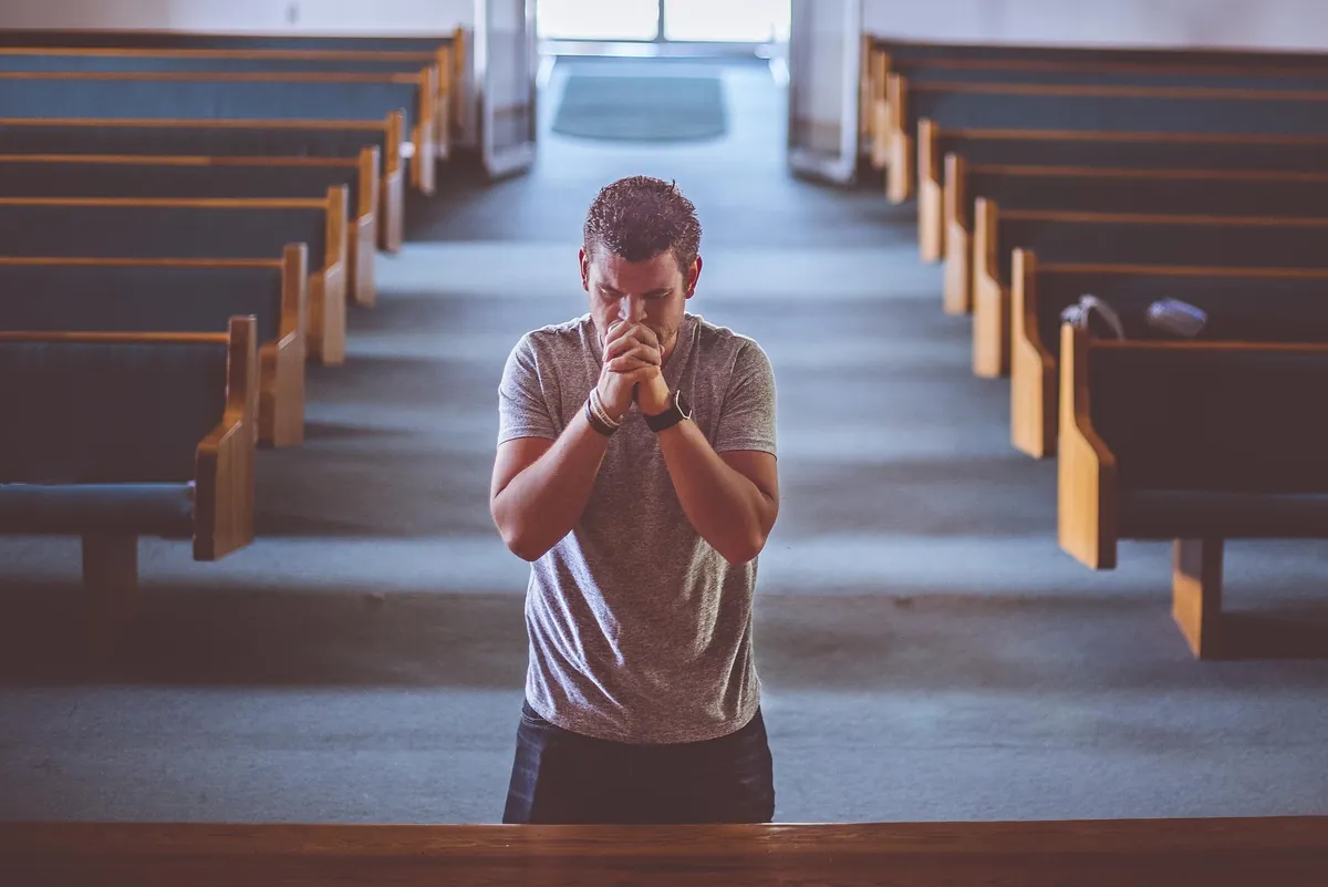Hombre orando solo, de rodillas, en una banca de iglesia vacía